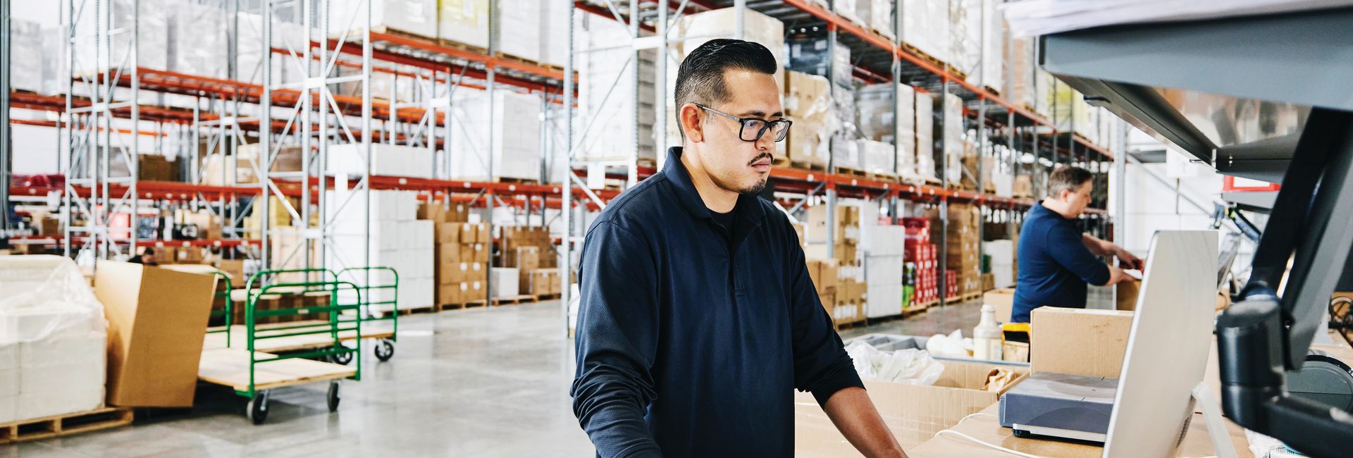 IT professional standing at a desk in a warehouse setting.